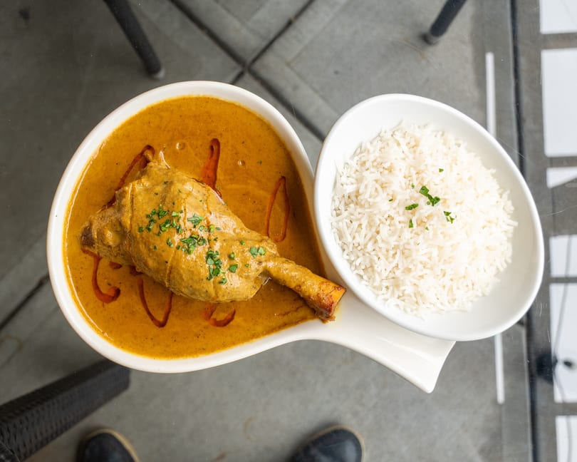 Lamb shank in a rich curry sauce with a side of white rice, garnished with herbs.