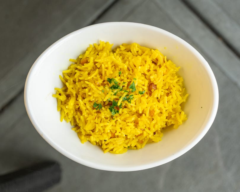 A white bowl filled with vibrant yellow rice, garnished with fresh green herbs.