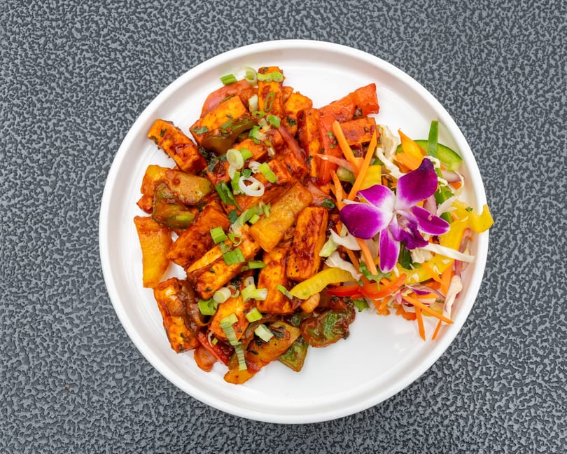 Chili Paneer, a spicy Indian dish with paneer, bell peppers, and onions, garnished with a purple orchid.