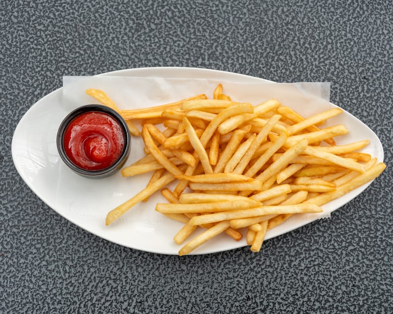 A white oval plate holds golden french fries with a side of ketchup on a dark textured surface.
