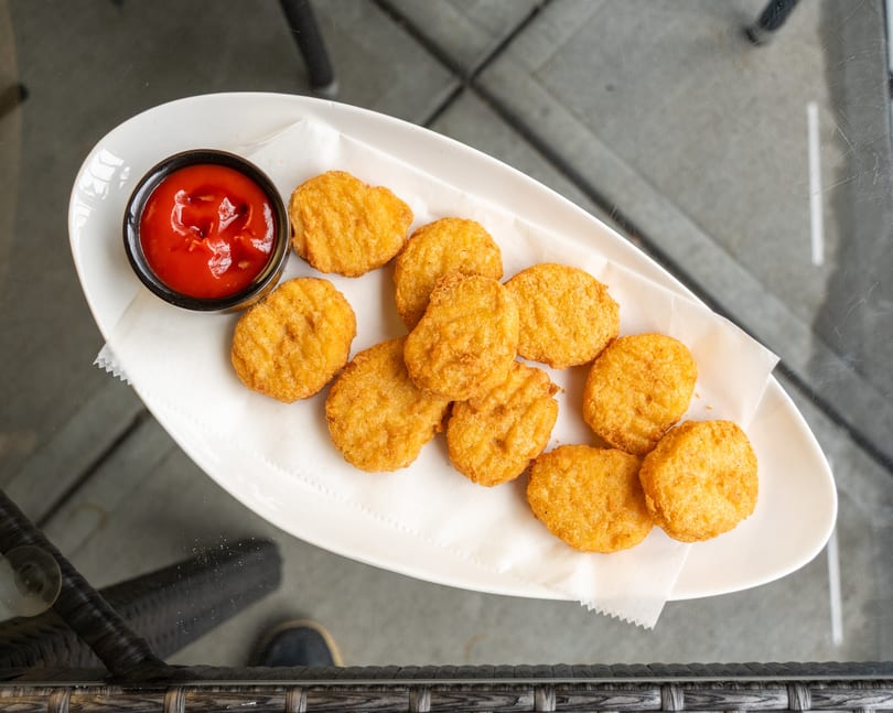 Golden-brown chicken nuggets with a side of ketchup on a white plate, viewed from above.