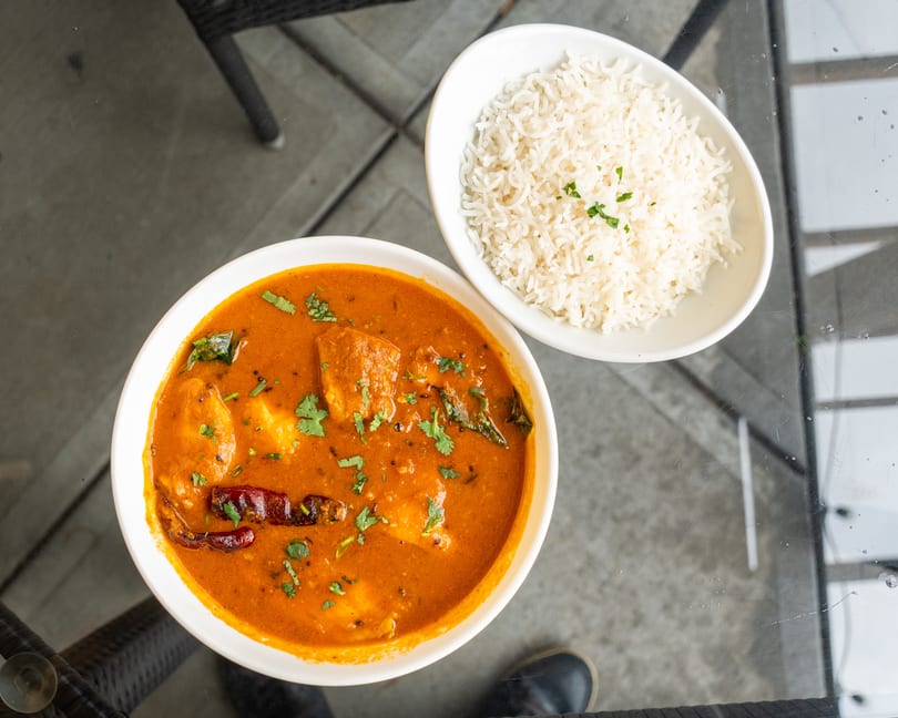 Overhead view of a bowl of orange curry with cilantro and dried chilies, next to a bowl of white rice.