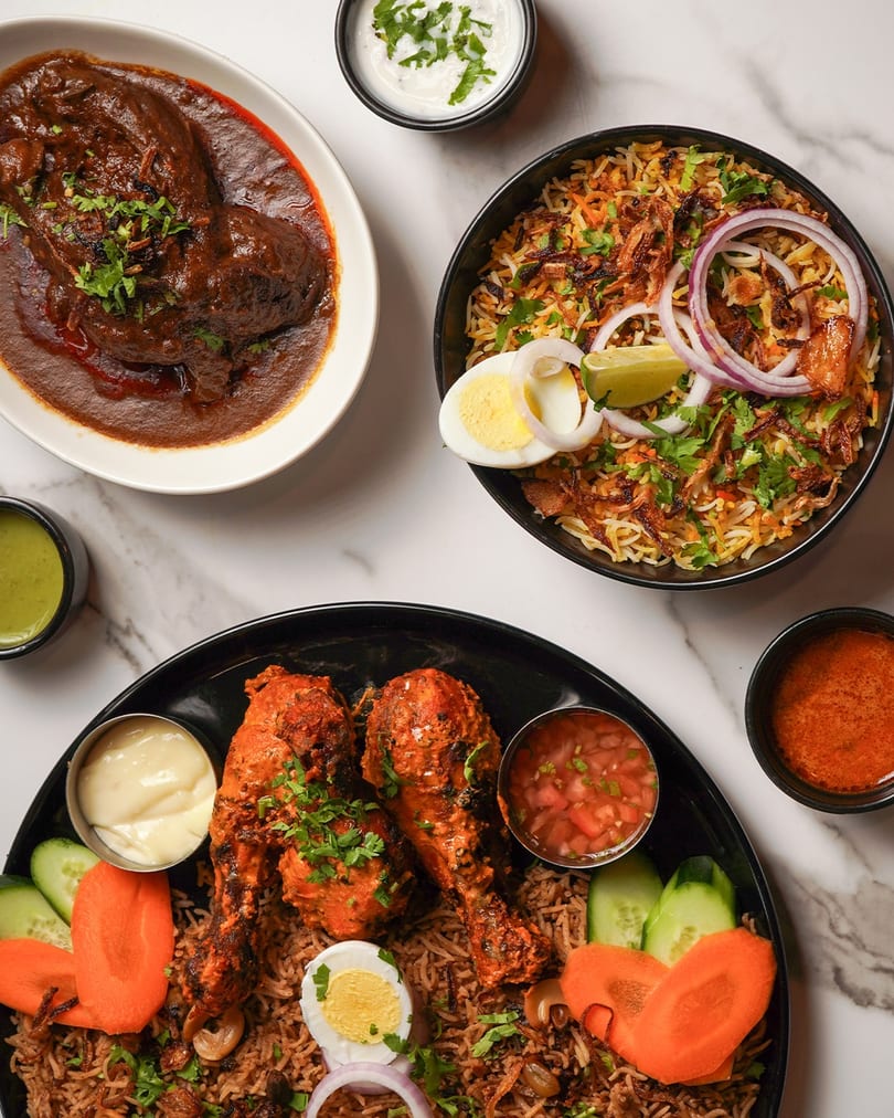 A top-down view of three Indian dishes: chicken curry, biryani, and roasted chicken legs with rice.