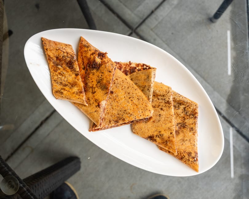 A white oval plate holds several triangular pieces of chocolate-dusted crepes on a glass table.