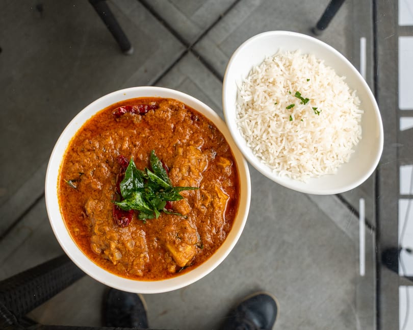 Overhead view of a bowl of orange curry with green garnish and a side of white rice.