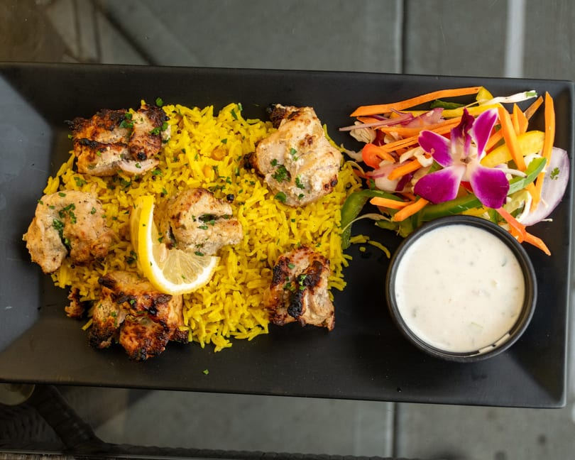 Chicken tikka with yellow rice, a side salad garnished with an orchid, and a dipping sauce.