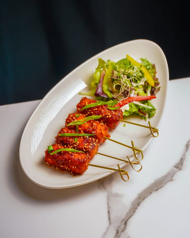 Four chicken skewers with sesame seeds and green onions, served with a side salad.