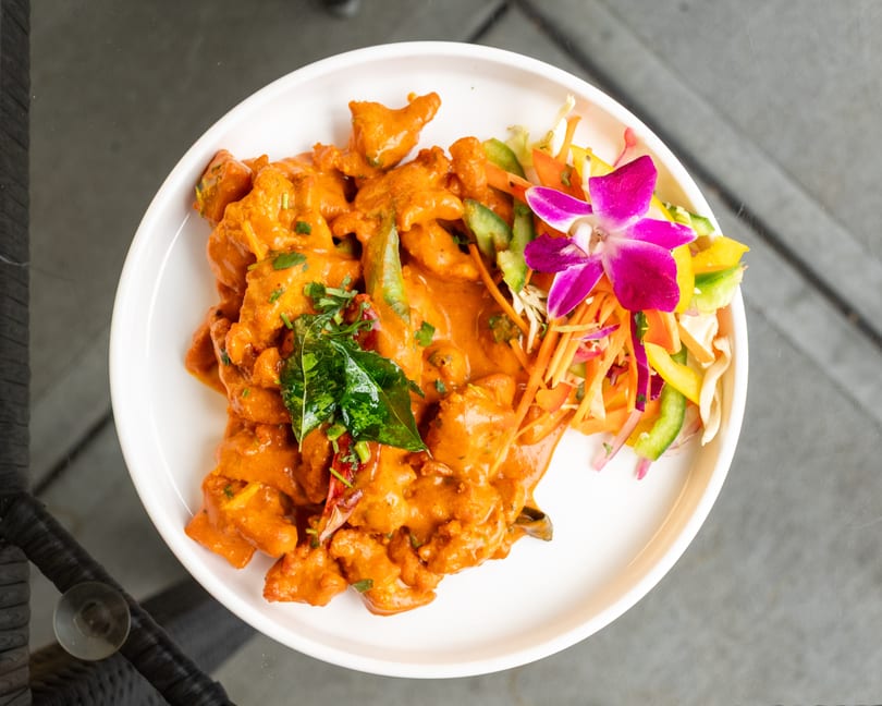 Chicken tikka masala with a side salad and purple orchid on a white plate.
