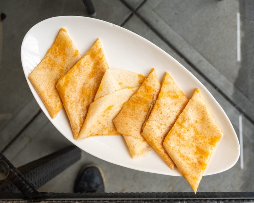 Overhead view of several triangular folded crepes with orange filling on a white platter.